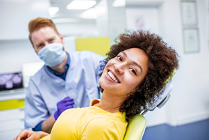  Smiling female patient sitting in dental chair with dentist in background