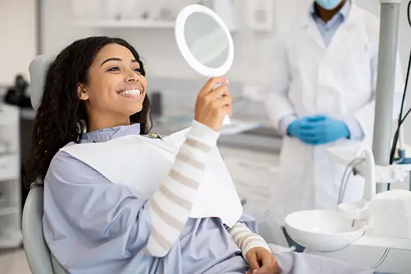 Beautiful patient looking in handheld mirror in dental chair