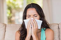 Woman with the flu blowing her nose ina  tissue