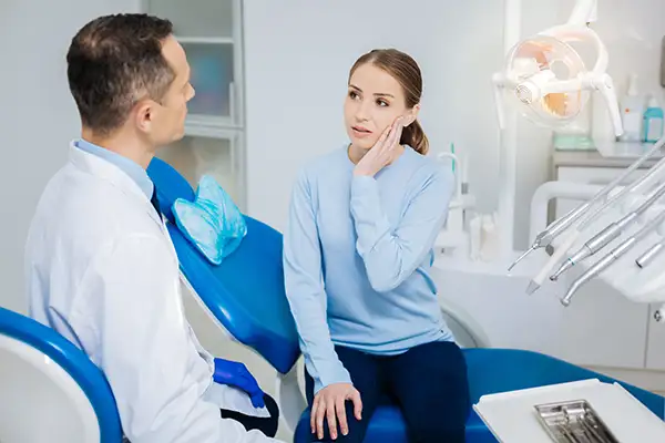 Concerned white patient discussing her tooth pain with her dentist while sitting in a dental chair at Singing River Dentistry.